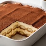 Best tiramisu recipe in white dish showing defined mascarpone layers and cocoa dusted top