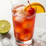 Classic rum punch in tall glass with orange slice cherry ice cubes and nutmeg garnish