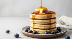 A stack of fluffy sourdough discard pancakes with melting butter and glistening maple syrup drizzle